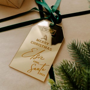 May include: Gold gift tag with the text "Merry Christmas Elsie, Love, Santa 2023" and a small gold sticker with the text "North Pole Delivery" and a reindeer graphic.