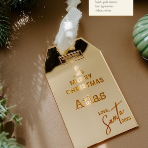 May include: Gold mirror Christmas ornament with the text "NORTH POLE DELIVERY", "MERRY CHRISTMAS", "Atlas", "LOVE, Santa", and the year "2023".