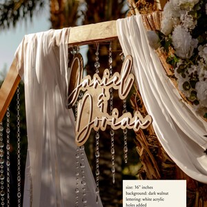 Puede incluir: Un letrero de boda de madera con los nombres "Daniel & Dorian" en escritura cursiva. El letrero tiene un tama&ntilde;o de 91,44 cm y un fondo de nogal oscuro con letras de acr&iacute;lico blanco. Se han a&ntilde;adido agujeros al letrero.