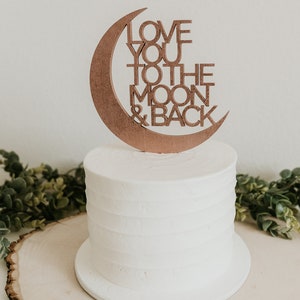 May include: A white cake with a wooden moon and back topper that says "Love you to the moon & back".