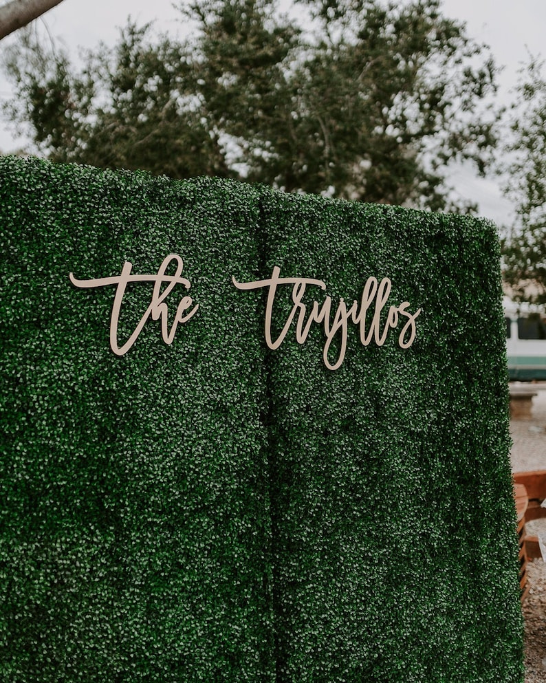 May include: A green artificial hedge backdrop with the words "the" and "Truillos" written in cursive on it.