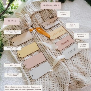 Op de afbeelding: Twee cr&egrave;mekleurige, grof gebreide kousen gepresenteerd met diverse rechthoekige cadeaulabels. De labels zijn verkrijgbaar in natuurlijke berk, goudspiegel, ros&eacute;goudspiegel en zilverspiegel afwerkingen, sommige met gegraveerde namen zoals Savannah en Grace.