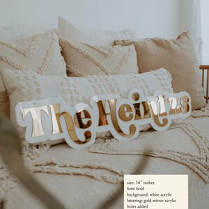 Puede incluir: Un letrero de acr&iacute;lico blanco con el texto "The Heinzs" en letras de acr&iacute;lico espejo dorado. El letrero mide 91,44 cm de largo y tiene agujeros a&ntilde;adidos.