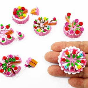 Puede incluir: Mini pastelitos rosas con glaseado blanco y decoraciones florales coloridas. Varios pasteles están enteros, mientras que otros están en rodajas, con piezas individuales esparcidas. Los pasteles están sobre blondas blancas.