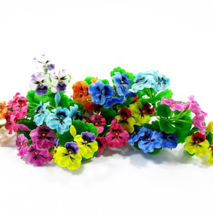 Puede incluir: Un ramo de flores de pensamiento artificiales que presenta una mezcla vibrante de colores, incluyendo pétalos amarillos, azules, rosas, naranjas, morados y blancos con centros oscuros, unidos a tallos verdes y pequeñas hojas verdes.