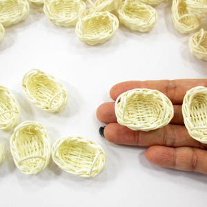 Adult hand holding two 1:12 scale miniature oval rattan baskets to show the elongated shape and high-quality artisanal weave.