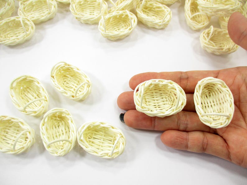 Adult hand holding two 1:12 scale miniature oval rattan baskets to show the elongated shape and high-quality artisanal weave.