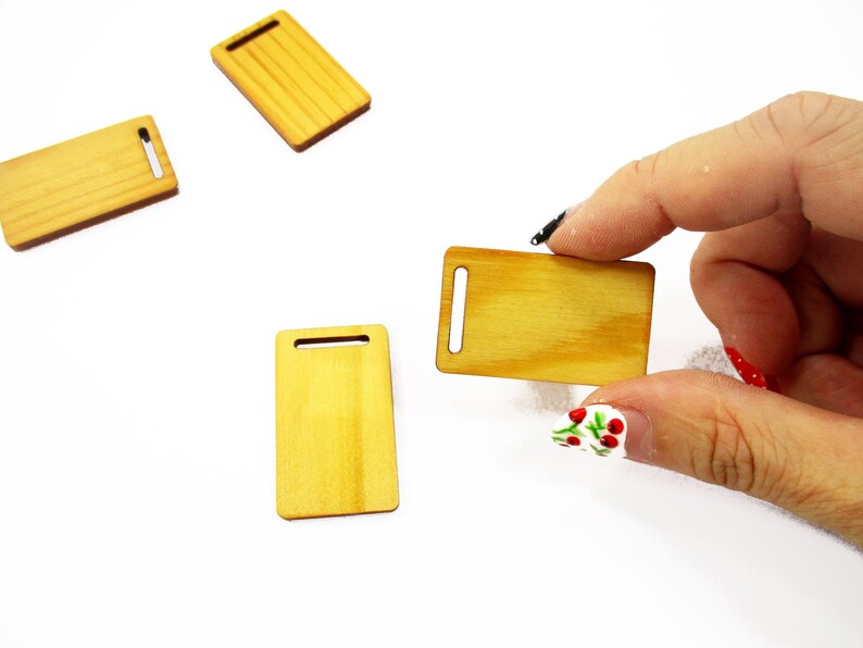 Fingers holding a handcrafted 1:12 scale miniature wooden board, showing detailed 23x38mm dimensions for dollhouse kitchens.