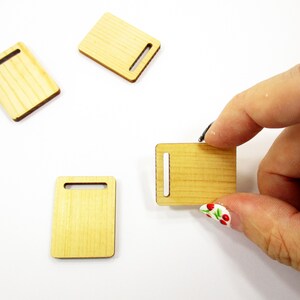 Fingers holding a tiny handcrafted 1:12 scale wooden cutting board to demonstrate the realistic small size for collectors.