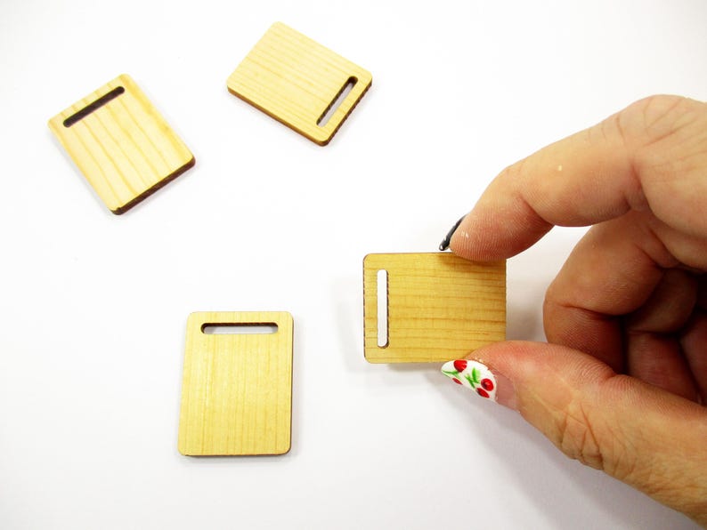 Fingers holding a tiny handcrafted 1:12 scale wooden cutting board to demonstrate the realistic small size for collectors.