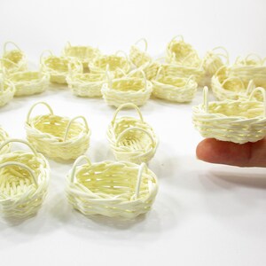 Adult finger holding the rim of a tiny 1:12 scale oval rattan basket with two side handles for dollhouse kitchen scenes.