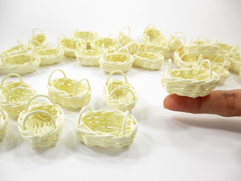 Adult finger holding the rim of a tiny 1:12 scale oval rattan basket with two side handles for dollhouse kitchen scenes.