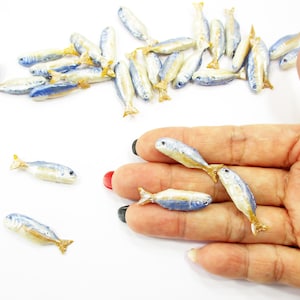 Peut inclure: Petits poissons miniatures avec des détails bleus et jaunes. Les petits poissons sont dispersés sur une surface blanche, certains sont tenus dans une main. Les poissons ont un design détaillé, avec un dessus bleu et des nageoires jaunes.