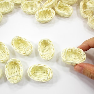 Fingertips picking up a tiny oval wicker basket to demonstrate the precise 1:12 scale realism for dollhouse bakery collectors.