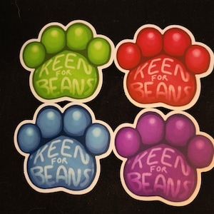 May include: Four paw print stickers with the text "Keen for Beans" in white lettering. The paw prints are green, red, blue, and purple.