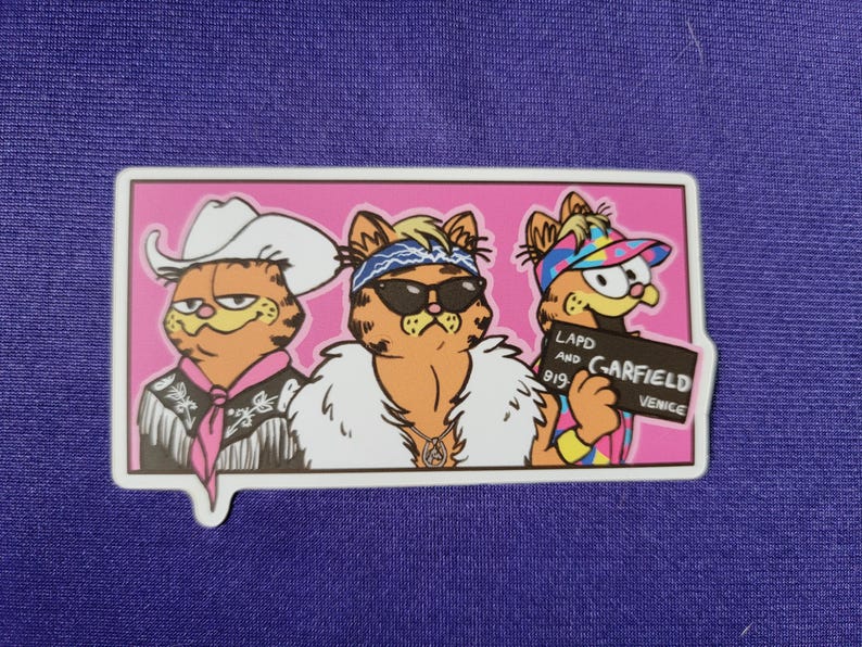 May include: A rectangular sticker on a purple background featuring three orange tabby cats in a pink frame. The left cat wears a white cowboy hat and fringed shirt. The middle cat wears sunglasses, a bandana, and a white fur coat. The right cat wears a colorful visor and holds a sign reading LAPD AND GARFIELD 919 VENICE.