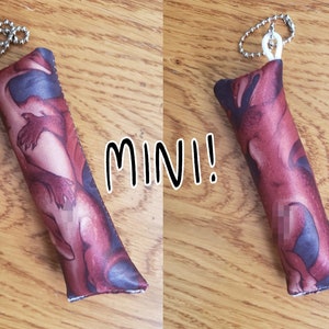 May include: A small, red and black fabric keychain with a dragon design. The keychain is attached to a silver chain. The text "MINI!" is written in black on a white background.