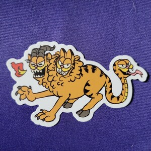 May include: A sticker featuring a mythical creature with two orange tabby cat heads and a snake tail. One head has goat horns and sharp teeth, while the other has a lion-like mane. The creature has a striped orange body, claws, and a small flame.