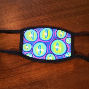 May include: A black face mask with a repeating pattern of blue, green, and purple eyes. The eyes have white pupils and yellow highlights.