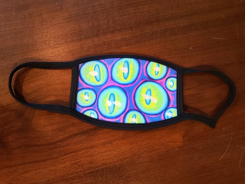May include: A black face mask with a repeating pattern of blue, green, and purple eyes. The eyes have white pupils and yellow highlights.