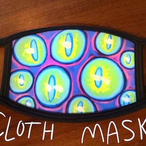 May include: A black cloth face mask with a colorful print of blue, green, yellow, and purple eyes. The mask has elastic ear loops.