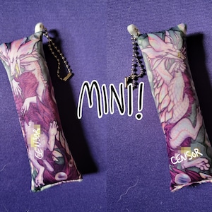 Può includere: Due portachiavi rettangolari in tessuto mini con un design a drago fantasy. I portachiavi hanno una catena e una parte superiore bianca. Il testo "MINI!" è in bianco e la parola "CENSOR" è stampata sul portachiavi.