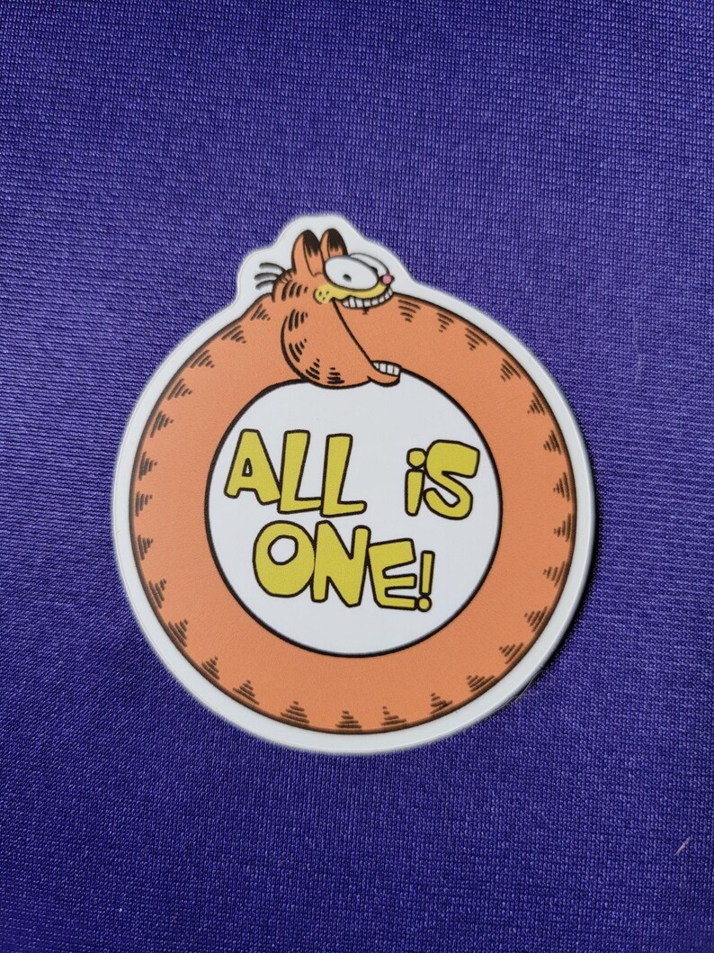 May include: A circular sticker featuring a cartoon orange cat biting its own tail to form a ring. The center is white with the yellow text ALL IS ONE! in a bold, blocky font. The cat has black stripes, a wide grin, and visible teeth.
