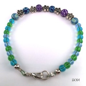 May include: A green, blue, and purple beaded bracelet with silver flower charms and a silver clasp. The bracelet has the number 15094 printed on the white background.
