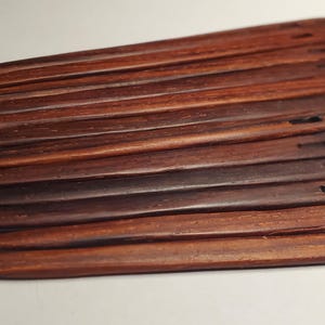 May include: A collection of dark brown wooden knitting needles. Each needle is long, slender, and tapers to a point at one end. The other end features a small, rectangular hole. The needles are arranged in a slightly overlapping pattern.