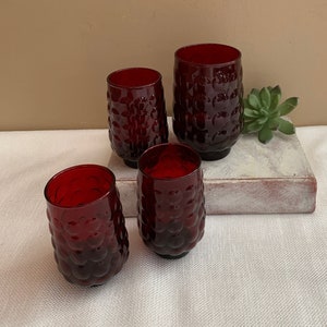 May include: Set of four red glass tumblers with a textured bubble design. The glasses are arranged on a white surface with a book underneath.