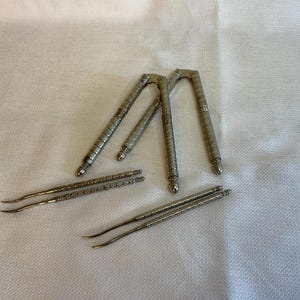 May include: A set of silver nutcrackers with intricate designs. The nutcrackers are in the shape of a V and have a pointed end. There are also two smaller silver tools with pointed ends.