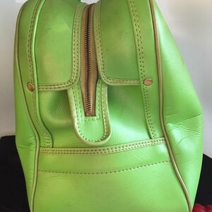 May include: A bright green leather travel bag with a zipper closure and gold hardware. The bag has a top handle and a smaller pocket on the front.