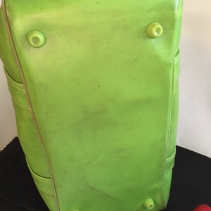 May include: A bright green leather duffel bag with four protective feet on the bottom.