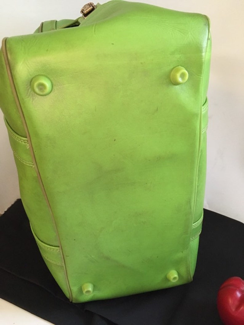 May include: A bright green leather duffel bag with four protective feet on the bottom.
