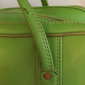 May include: Close-up of a bright green leather travel bag with a top handle and two brass rivets. The bag has a light brown trim and stitching.