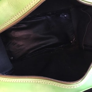 May include: A bright green leather travel bag with a zipper closure and a black fabric lining. The bag is open and the interior is visible.