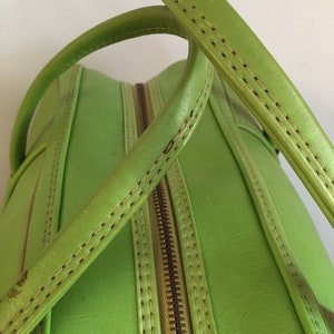 May include: A bright green leather handbag with a zipper closure and double top handles. The handles are stitched with a contrasting light brown thread.