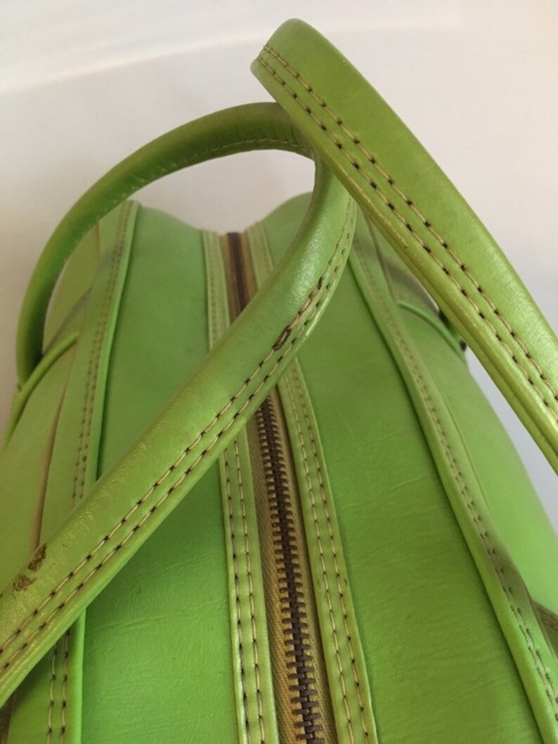 May include: A bright green leather handbag with a zipper closure and double top handles. The handles are stitched with a contrasting light brown thread.