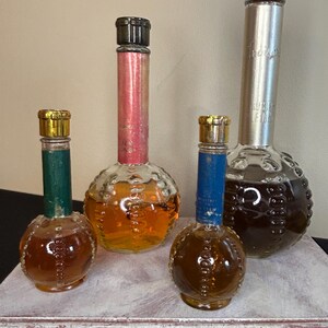 May include: Four vintage glass bottles with textured round bodies and different colored caps. The bottles contain a brown liquid and are arranged on a white surface.