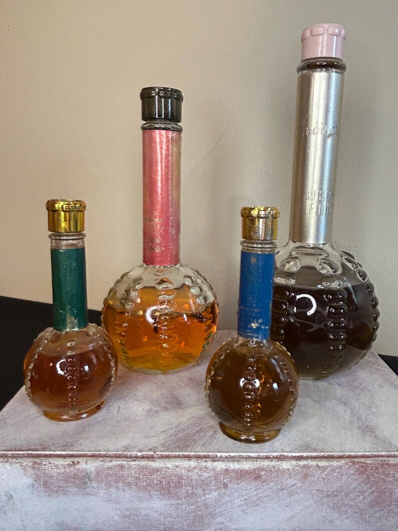 May include: Four vintage glass bottles with textured round bodies and different colored caps. The bottles contain a brown liquid and are arranged on a white surface.