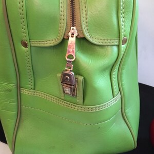 May include: A bright green leather travel bag with a zipper closure and a metal lock. The bag has a brown zipper and stitching.