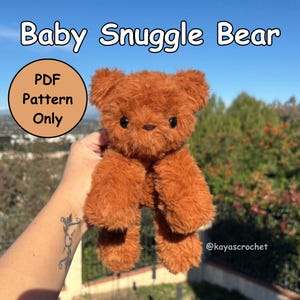 Puede incluir: Un osito de peluche marrón con ojos negros de botón y una textura suave. El texto "Baby Snuggle Bear" está en la parte superior, con "PDF Pattern Only" en un círculo. El oso se sostiene contra un fondo de vegetación y cielo azul.