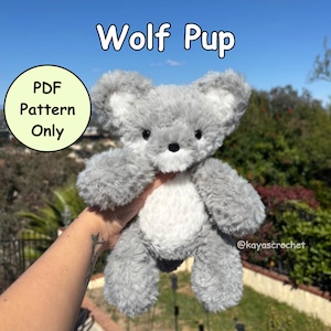 May include: A soft, grey and white wolf pup toy with a black nose and eyes. The text "Wolf Pup" is above the toy, and "PDF Pattern Only" is in a circle on the left. The toy is held up against a background of green foliage and a blue sky.