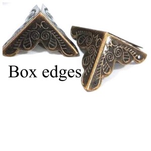 Puede incluir: Dos protectores de esquina de metal dorado adornados con un dise&ntilde;o floral decorativo. Bordes de caja.