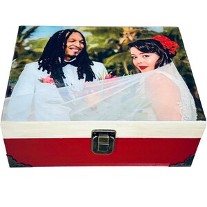 May include: A red wooden box with a white lid and a brass latch. The lid features a printed photo of a couple in wedding attire, with the bride wearing a white veil and the groom wearing a white suit and a black bow tie.