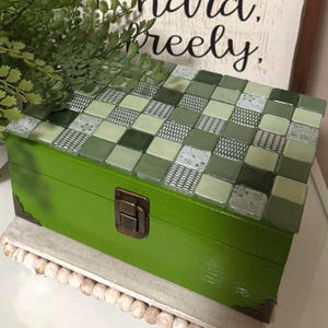 May include: Green wooden box with a mosaic tile lid. The tiles are various shades of green and white. The box has a brass latch.