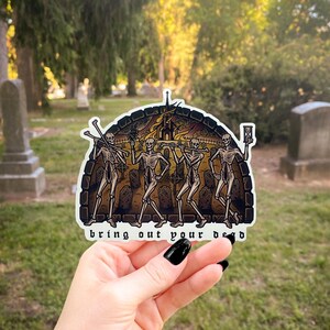 May include: A die-cut sticker featuring an illustration of four skeletons walking through a graveyard with a burning church in the background. The skeletons carry bones and an hourglass. The text "bring out your dead" is printed at the bottom.