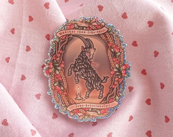 May include: A holographic sticker featuring a black goat standing on its hind legs inside an oval frame decorated with wheat and berries. A lit candle sits below the goat. The text reads, "wouldst thou like to... live deliciously?"
