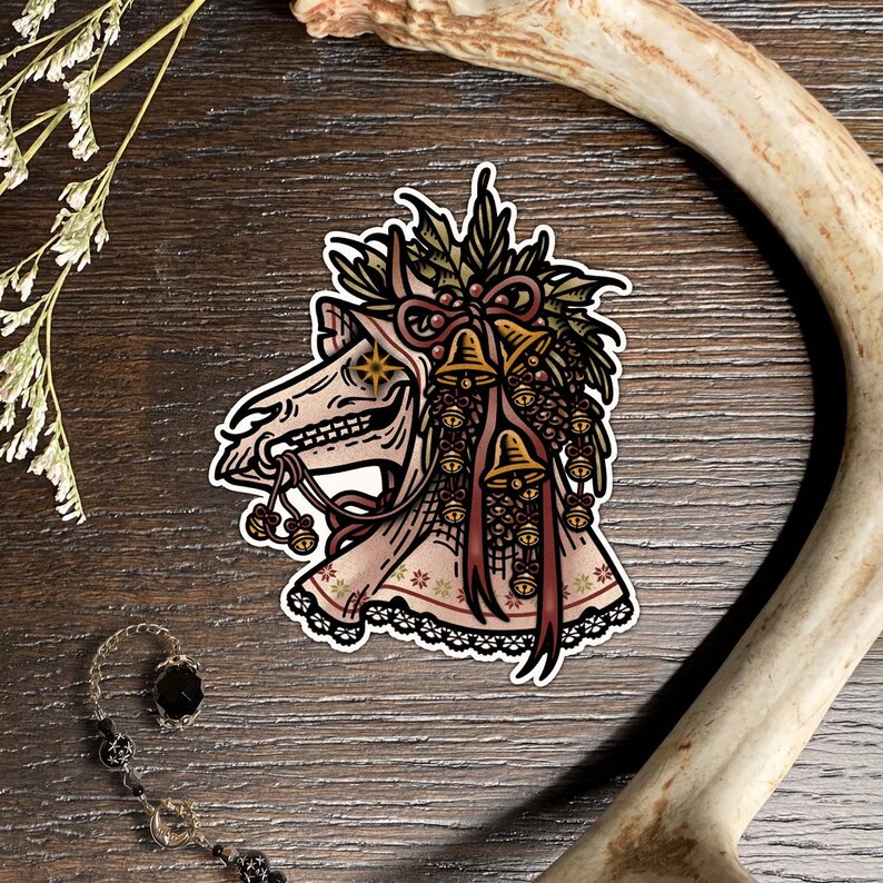 May include: A sticker featuring a horse skull adorned with a festive wreath of holly, pinecones, and golden bells. The skull has a star-shaped eye, a bridle with small bells, and a decorative fabric covering with a lace trim and snowflake pattern.