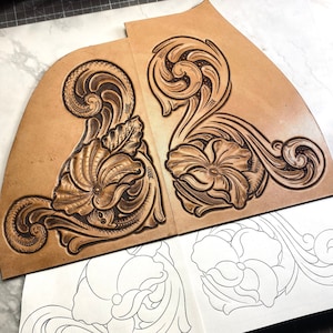 May include: Two pieces of brown leather with intricate floral designs carved into the surface. The designs feature a large flower with swirling leaves and stems. The leather is laid out on a white surface with a pencil drawing of a similar design.